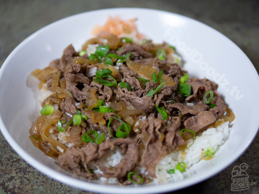 A large bowl of Japanese beef over rice (Gyudonburi - beef rice bowl) is topped with sliced green peppers and complimented with pickled ginger