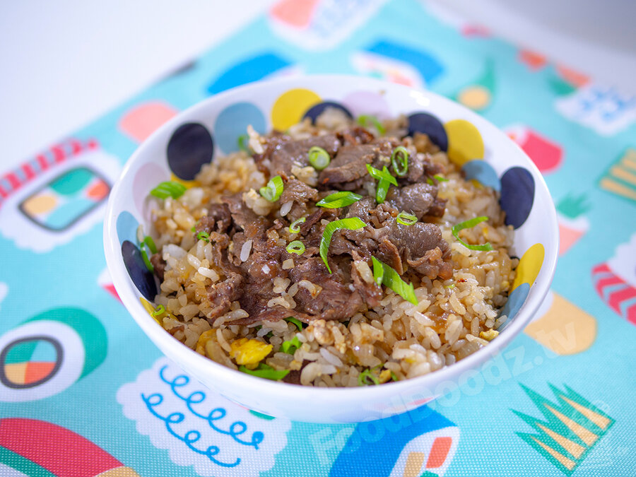 Bowl of gyudonburi fried rice (a leftover remix recipe) sits in bowl with bright pattern topped with slices of green onion. An illustrated sushi themed placemat sits underneath