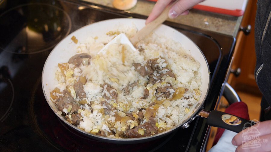 Incorporating rice with beef, eggs, and onions by stirring with spatula