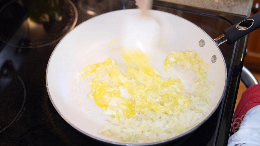Using spatula to mix scrambling eggs into onion