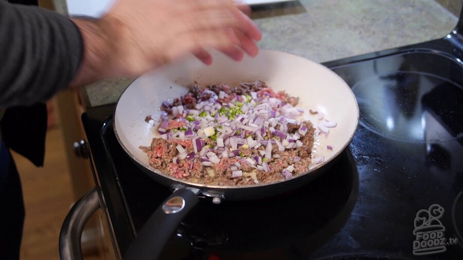 Chopped red onion and serrano are added to ground beef in pan