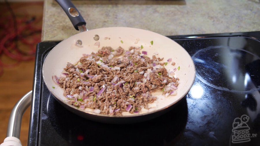 Browned ground beef, red onion, and serrano sits toasting skillet