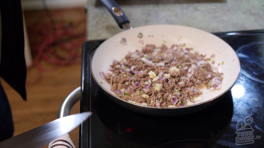 Minced garlic is added to ground beef, red onion, and serrano in skillet