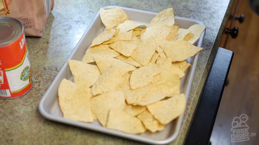 Tortilla chips are spread out evenly over sheet pan