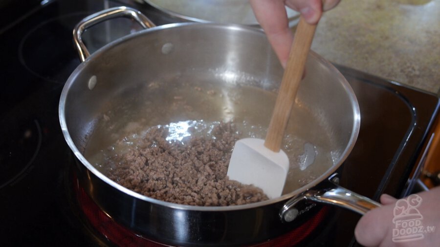 Ground beef is browned in large pan while being stired by large spoon