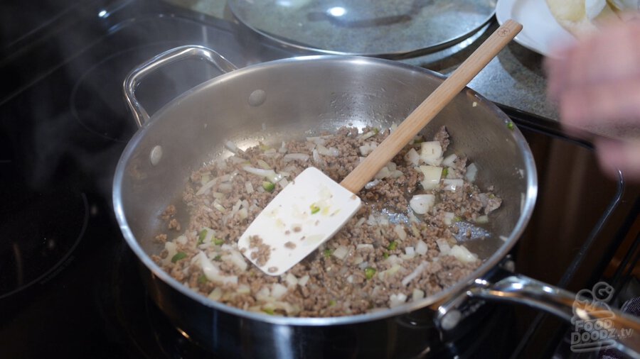 Chopped onion and serrano peppers are added to browned ground beef in large pan