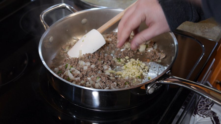 Minced garlic is added to ground beef, onion, and serrano in pan