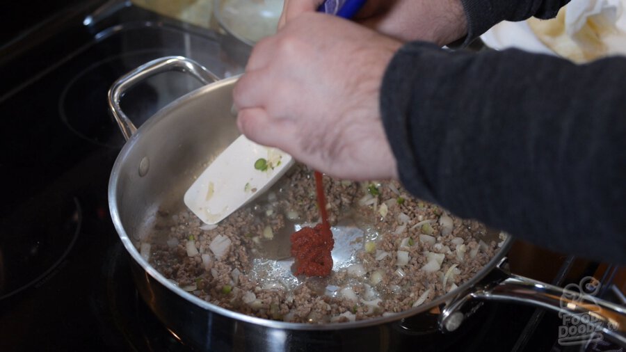 Tomato paste is squeezed from tube into pan with ground beef, onions, and peppers