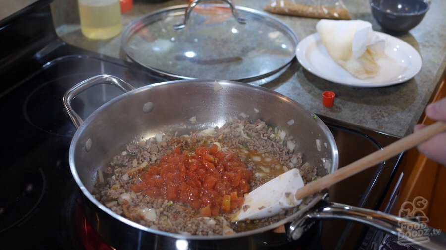 A can of rotel is added to pan of beef, onion, and peppers