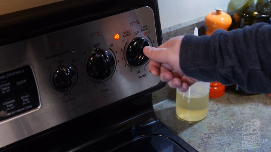 Hand reaches up to stove control panel to turn burner knob to low