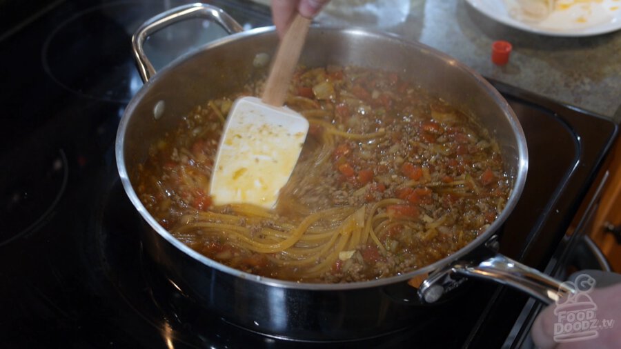 After lid is removed from pan, a large spoon is used to stir spaghetti mixture