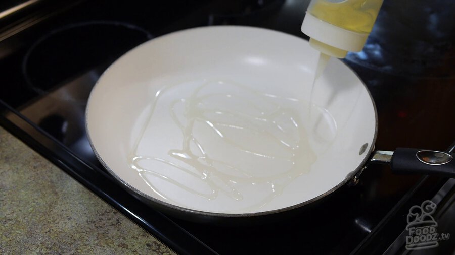 Vegetable oil is squeezed from bottle around non-stick skillet