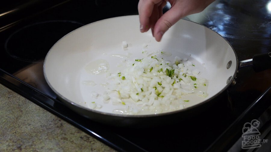 Chopped onion and serrano pepper is added to oiled non-stick skilled to saute