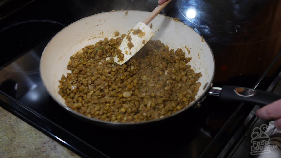Large spoon is used to stir thicken lentil mixture in skillet