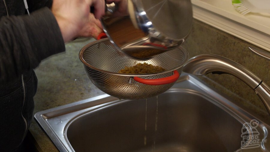 Pot of lentils is dumped into colander and drained over sink