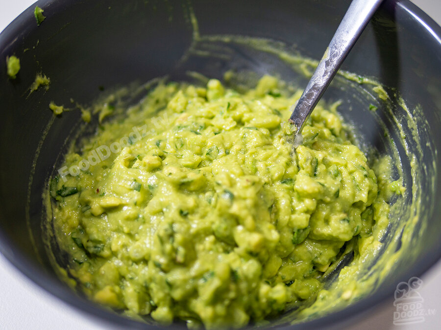 Bright green guacamole in dark gray bowl with spoon raise scoop up. Looks delicious!