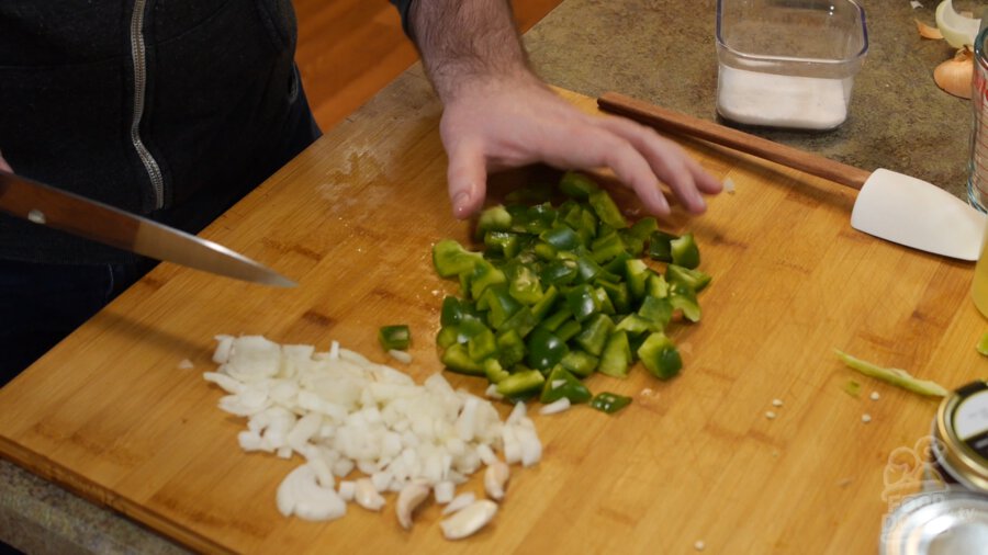 Green bell pepper and onion chopped on wood cutting board by chef's knife