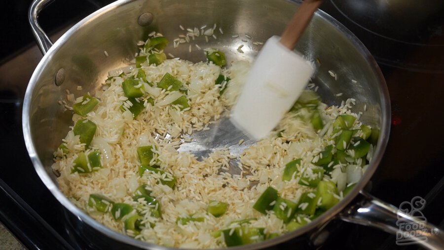 Chopped green bell peppers and onions are added to pan of toasted white rice