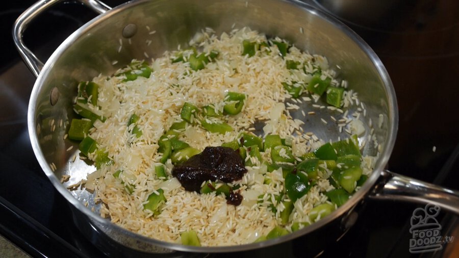 Large dollop of liquid vegetable broth concentrate is added to pan of toasted rice