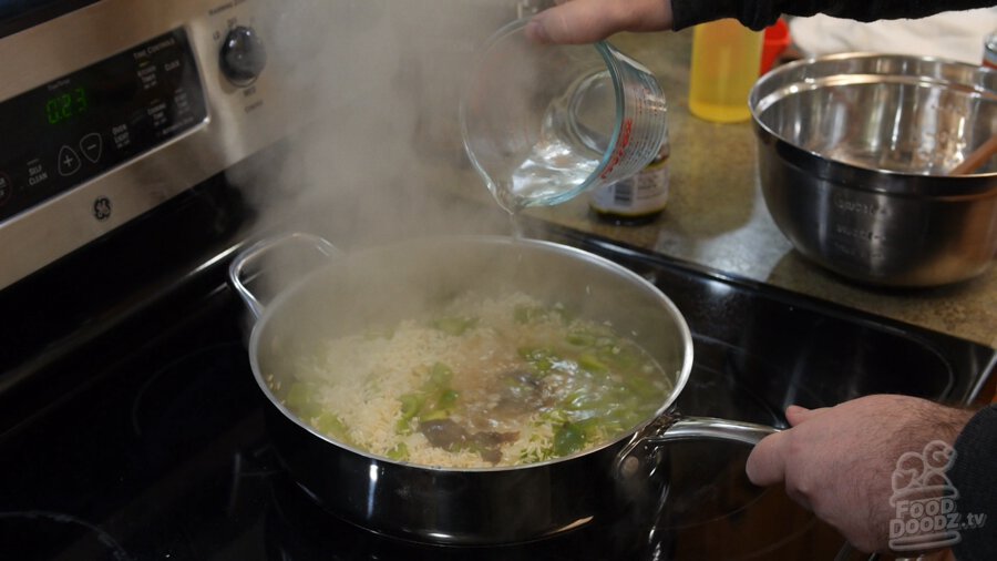 Water is poured from a measuring cup to pan of toasted rice while sizable steam cloud rises