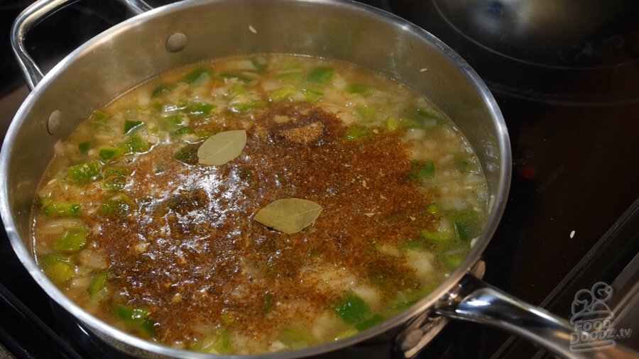 Bay leaves and taco seasoning sit on top of vegetable broth, green bell pepper, onion, and toasted rice mixture