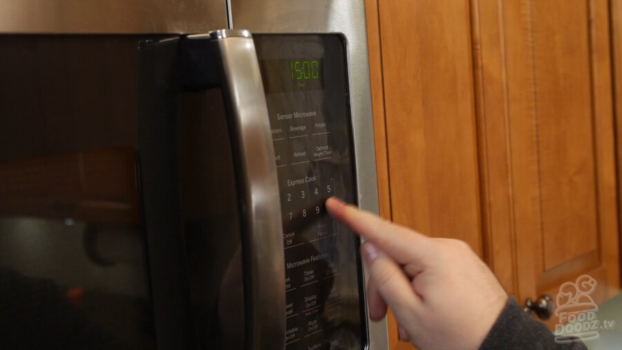 Hand presses button on microwave to set timer for 15 minutes