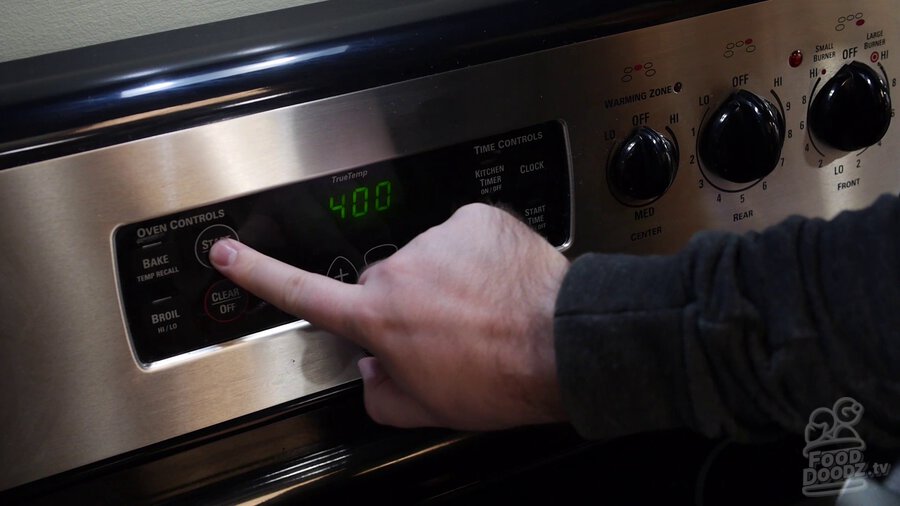 Hand presses button on oven control panel to power on to 400 degrees
