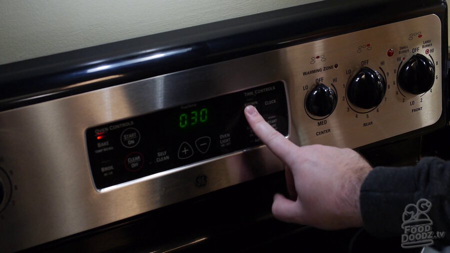 Hand presses button on oven control panel to set timer for 30 minutes
