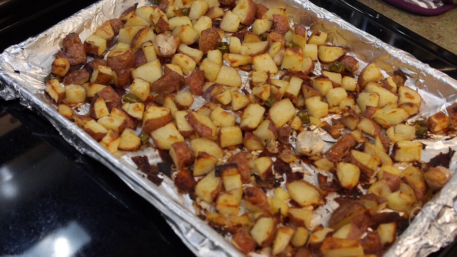 Completed roasted potato sheet pan is removed from oven and sat on top. Everything is golden brown and crispy.