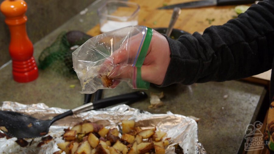 A hand placed inside a plastic sandwich bag is used to grab roasted garlic cloves and squish out garlic from wrapper to keep hands from smelling like garlic for the rest of your life.