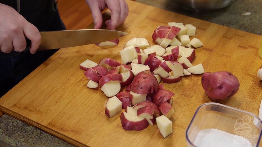 Slicing red potatoes into cubes on wooden cutting board