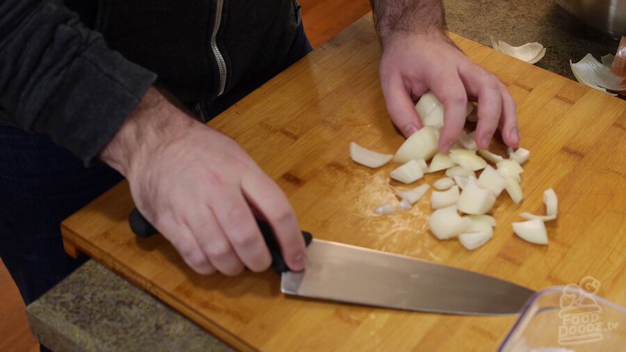 Onion chopped into large chunks by chef's knife on cutting board