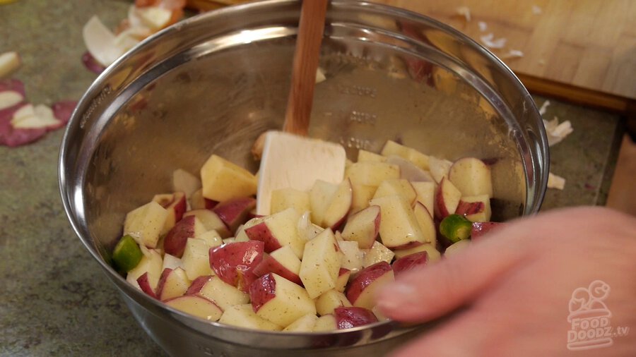 Using large spoon to toss potatoe, serrano pepper, and onion mixture to fully coat everything in oil and pepper