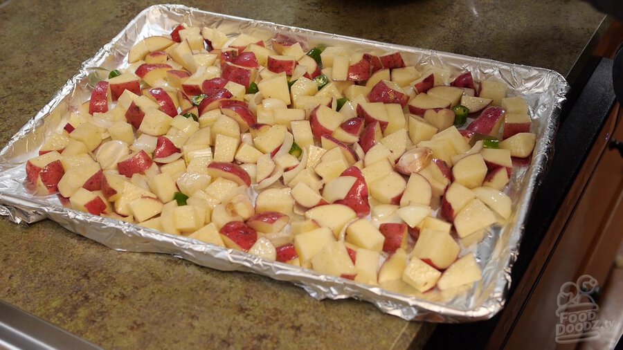 potato, serrano pepper, and onion mixture spread out flat onto tin foil lined baking sheet