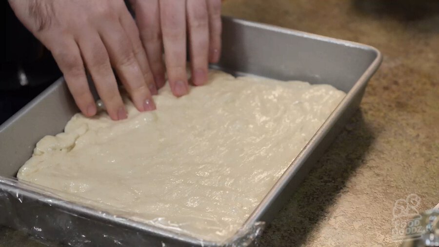 Using your hands to work pizza dough back into corners of sheet pan to try and flatten it back out the best you can