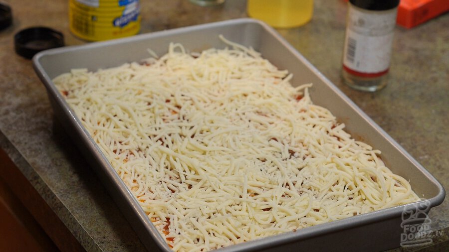 A nice healthy covering of cheese atop a pizza dough in a sheet pan