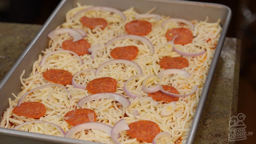 Pepperoni and onion slices top pizza in sheet pan