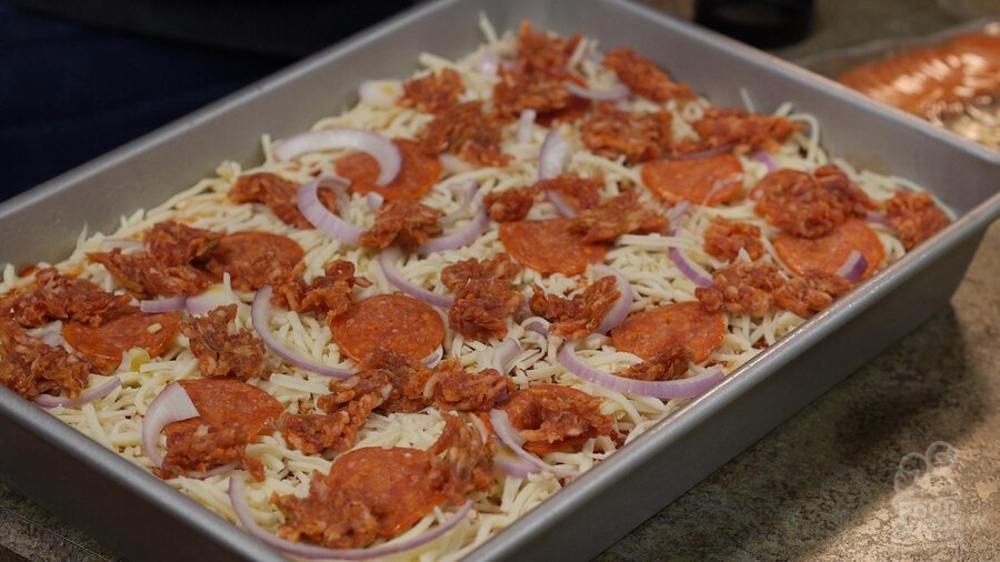 Small chunks of Italian sausage cover pizza in sheet pan