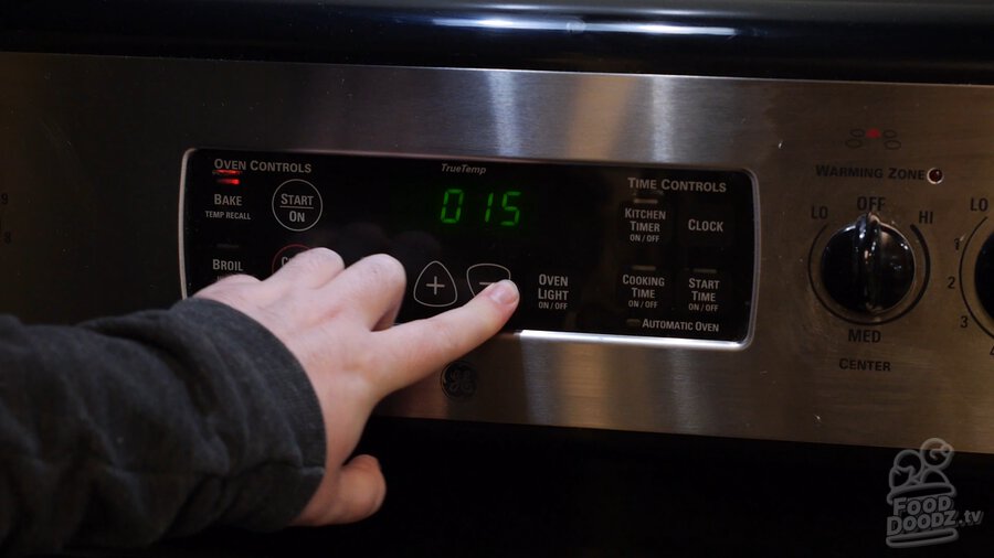 Hand presses button on oven control panel to set timer for 15 minutes