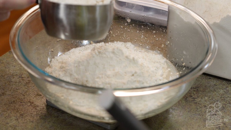 Scooping flour into glass mixing bowl resting on digital scale