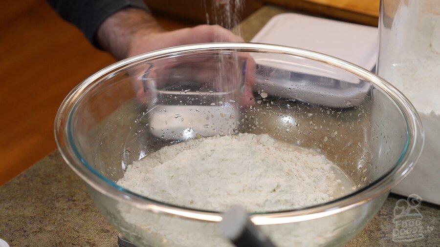 Sprinkling salt into large glass mixing bowl on top of digital scale