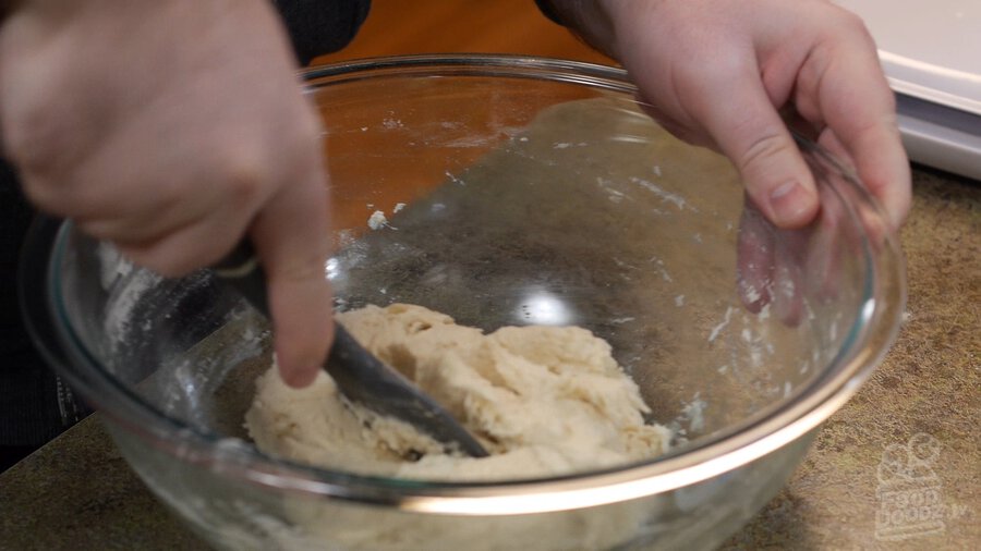 Using large spoon utensil to incorporate mixture into pizza dough in large glass mixing bowl