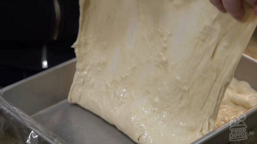 Lifting pizza dough by two corners and folding it over on top of itself (lengthways)