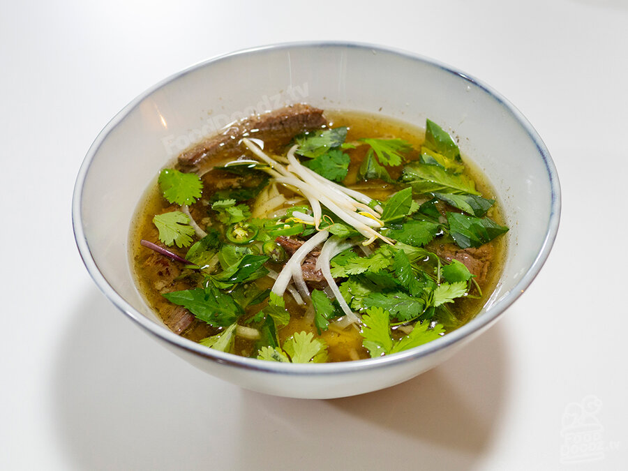 Gigantic bowl of fresh homemade Vietnamese Pho Beef Noodle Soup made from scratch in an Instant Pot with bone broth and topped with beansprouts, cilantro, sliced serrano chili peppers, and Thai basil