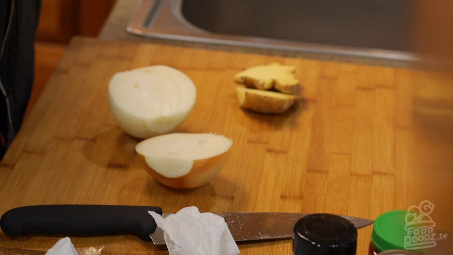 Onion and ginger root sliced in half on cutting board with chef's knife