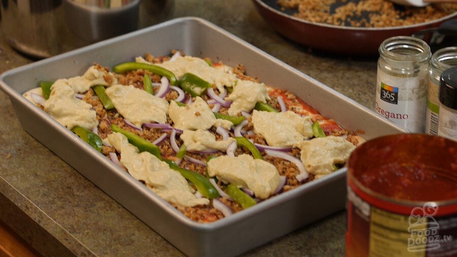 Dollops/large spoonfuls of homemade vegan cashew cheese top pizza in sheet pan