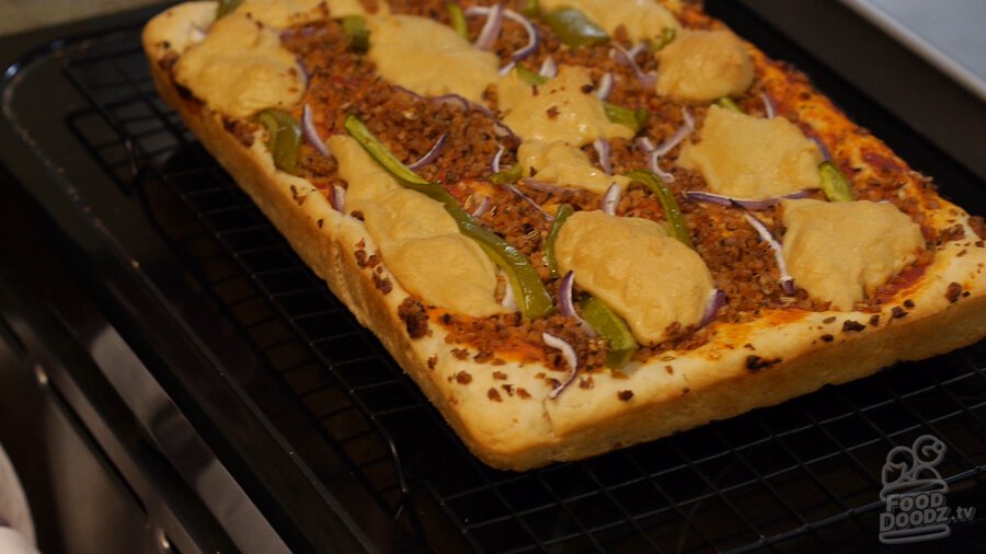 Completed golden brown and delicious (GBD) radical vegan pizza with Italian textured vegetable protein (TVP) sausage and homemade vegan cashew cheese sits on drying rack to cool after being removed from oven and sheet pan