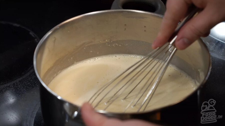 Cashew puree being heated over low heat in sauce pan. Stirring with whisk.