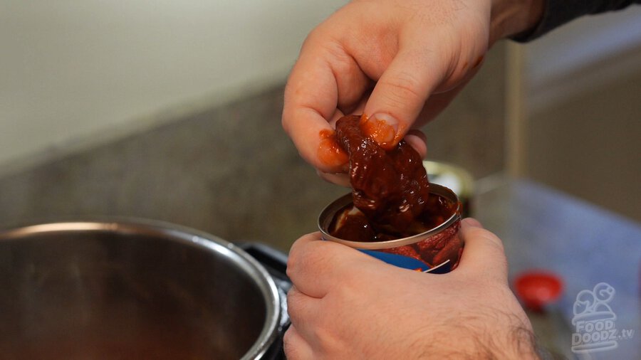 Hands grabbing chipotle chiles out of can with adobo sauce on fingers