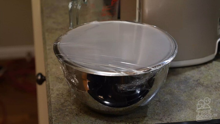 Placing saran plastic wrap over bowl of microwaved chilies in water